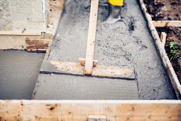 Mason building and leveling a first layer of fresh concrete floor at house stairs and sidewalks, construction site