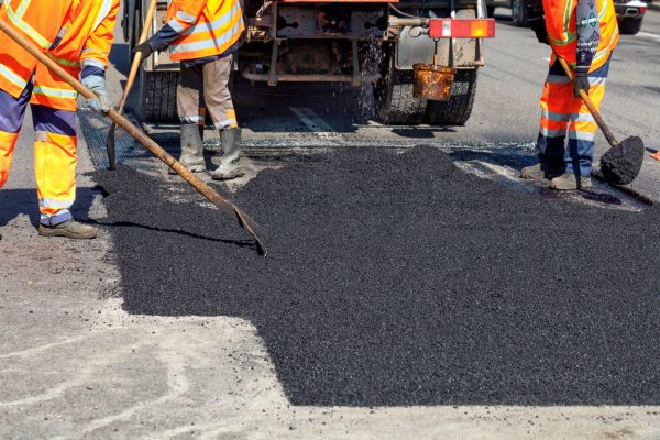 The road workers updating part of the road with fresh hot asphalt and smoothes it for repair